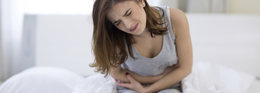 Young woman sitting on the bed with pain nj doctor abdominal pain expert